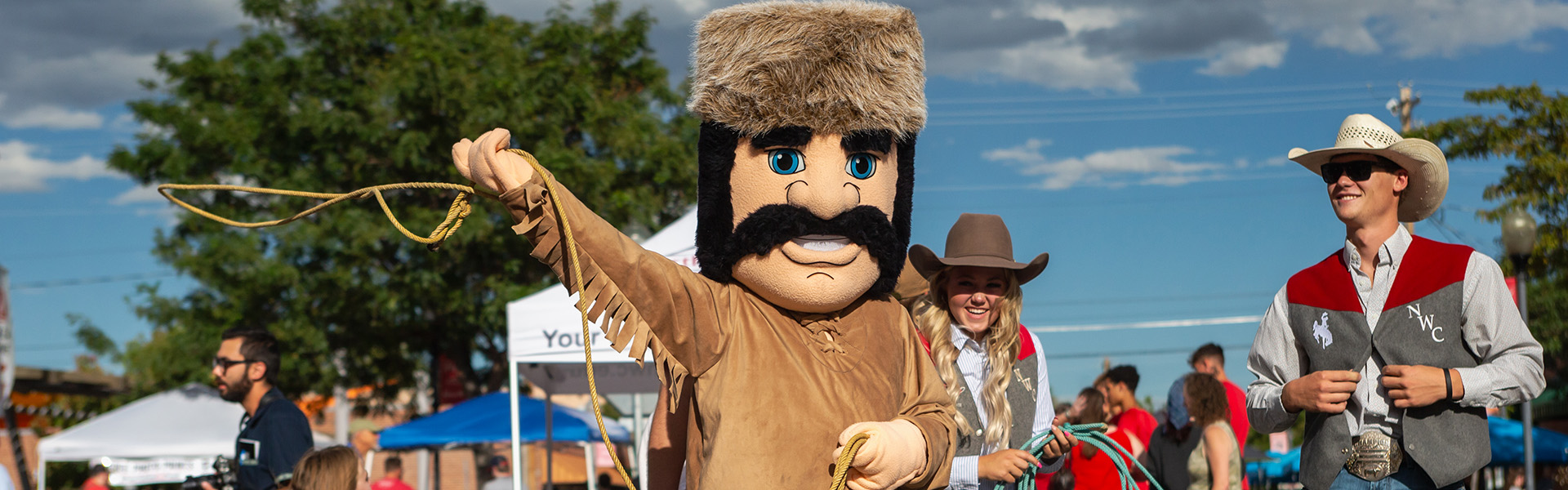 Trapper mascot twirling a lasso with rodeo student athletes watching