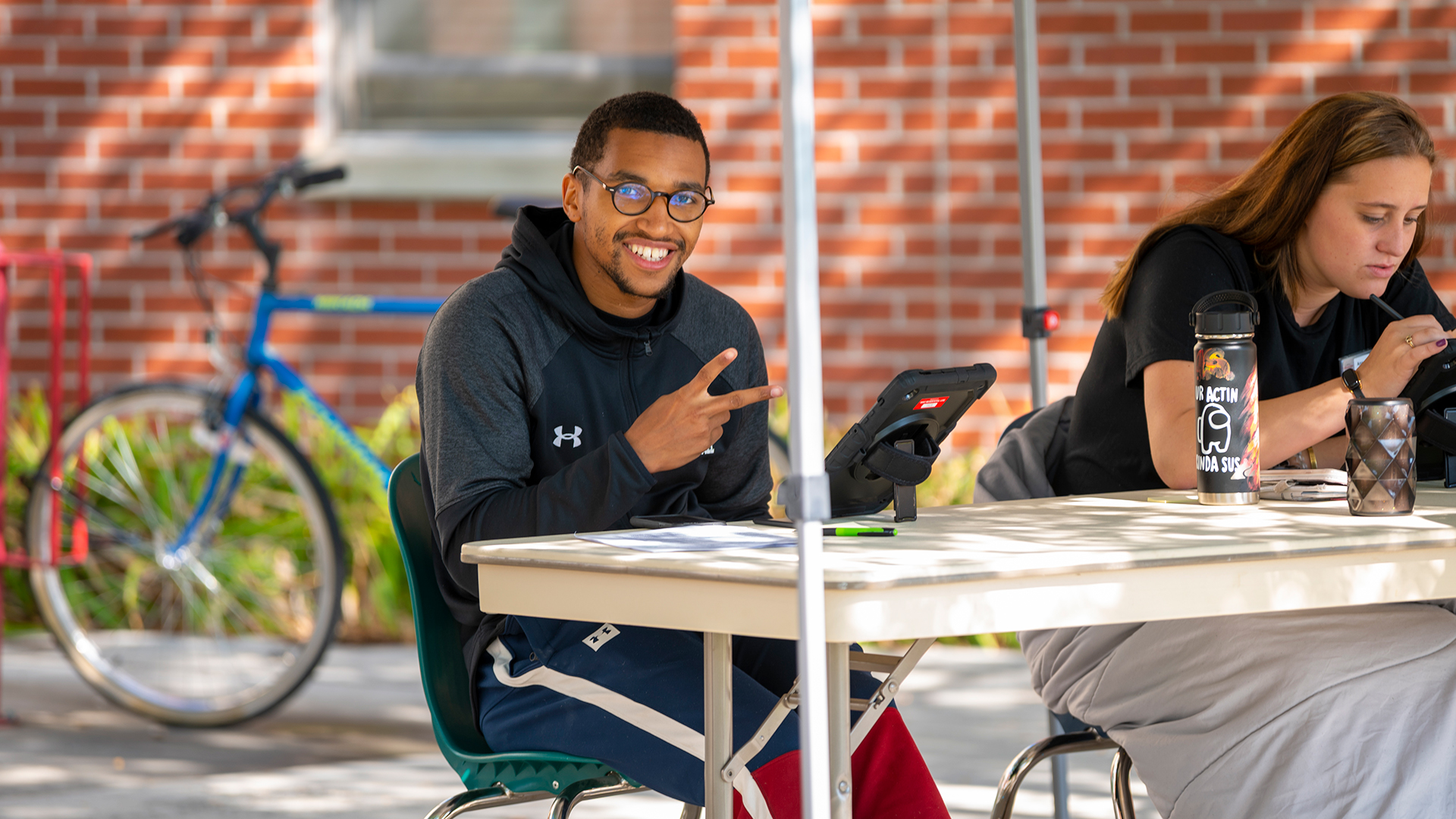 Make student sitting behind an outdoor table smiling