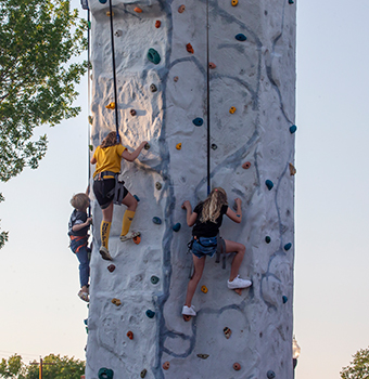 Three children climbing an outdoor rock wall at sunset