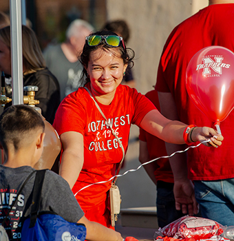 A smiling woman handing a balloon to a boy