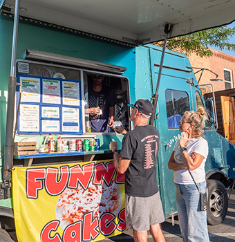 A man and woman ordering funnel cakes from a food truck`