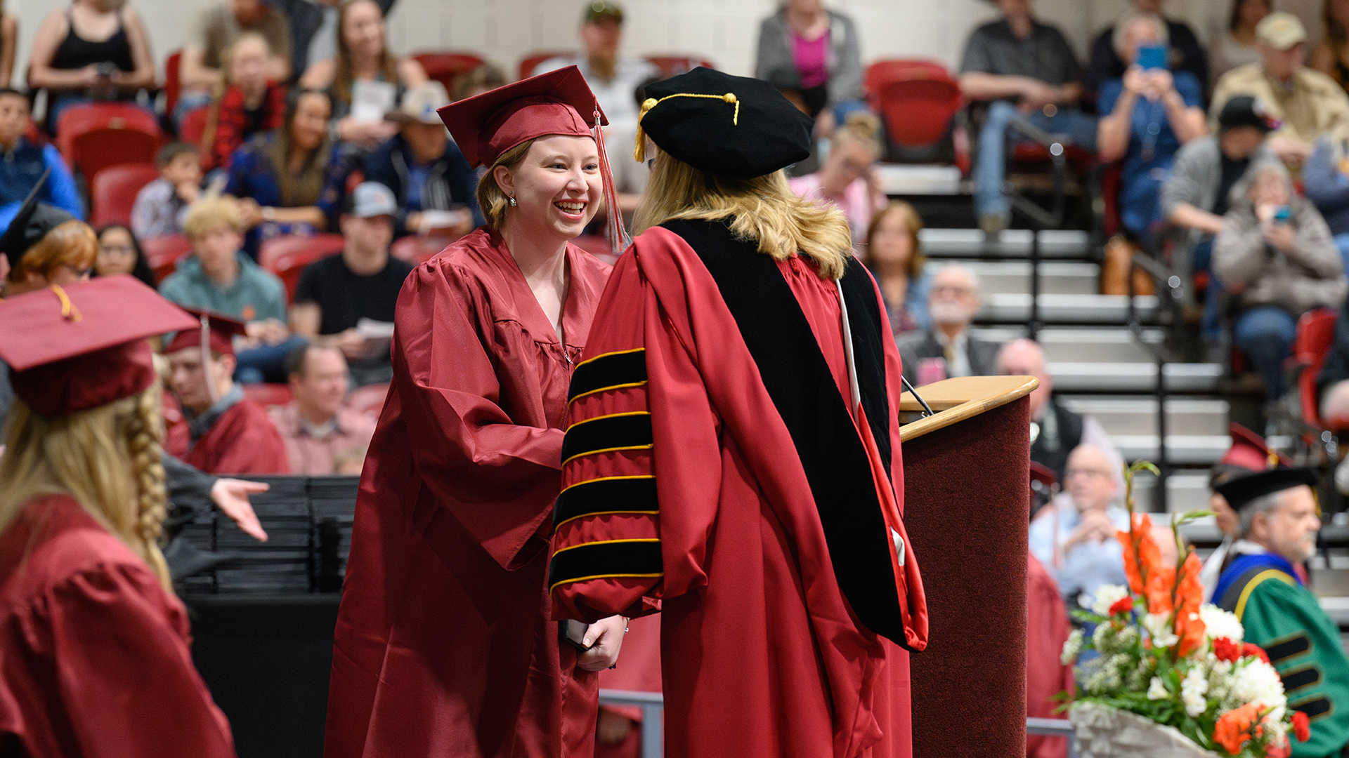 Smiling female student in cap and gown shaking hands with the college president on stage