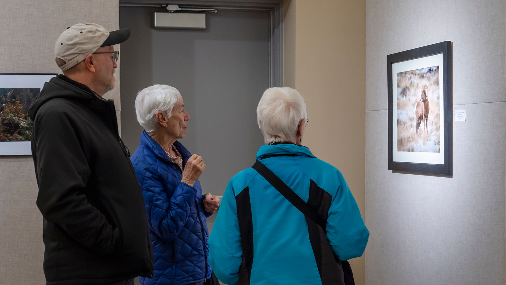 Three people, two women and one man, standing in front of a photo on a wall inside a gallery