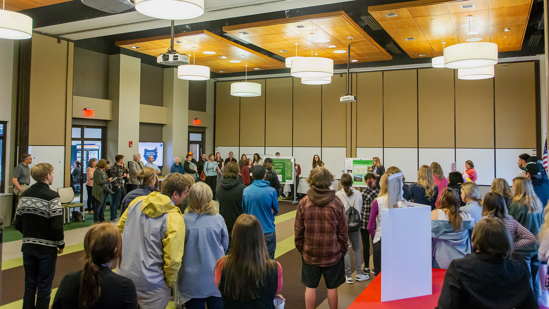 A large group of people standing in a conference room listening to someone speak