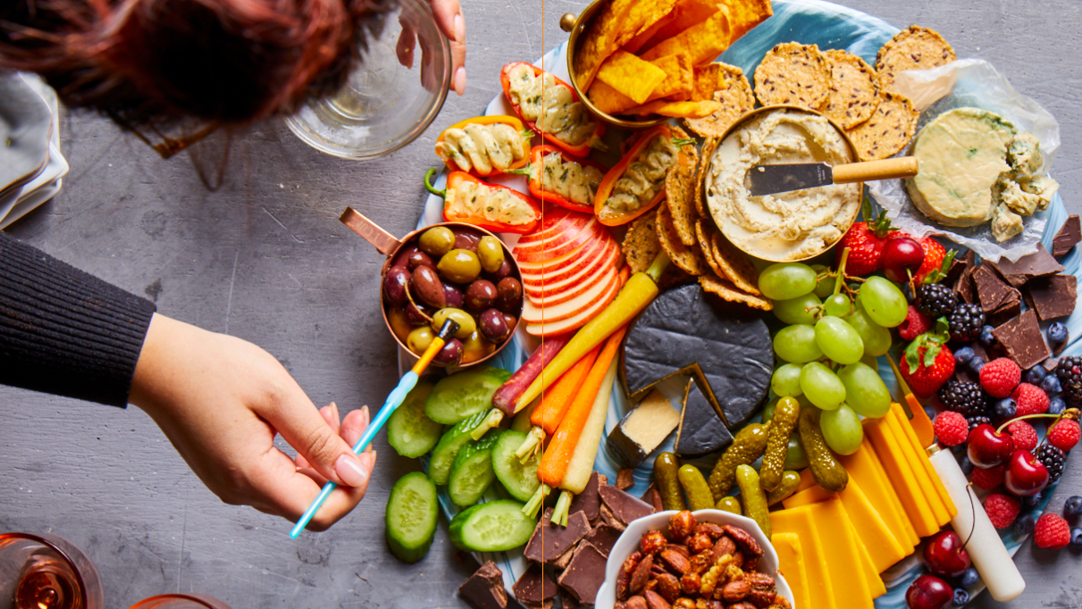A circular plate filled with cheeses, fruit, crackers and other small foods