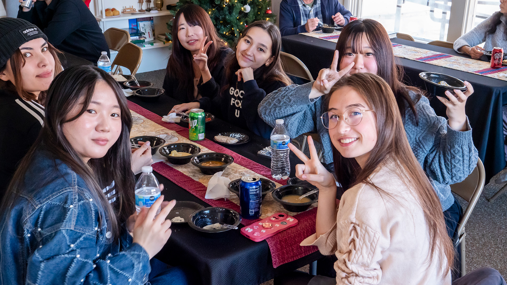 A group of six female college students sitting around a table with soup bowls, smiling and looking at the camera