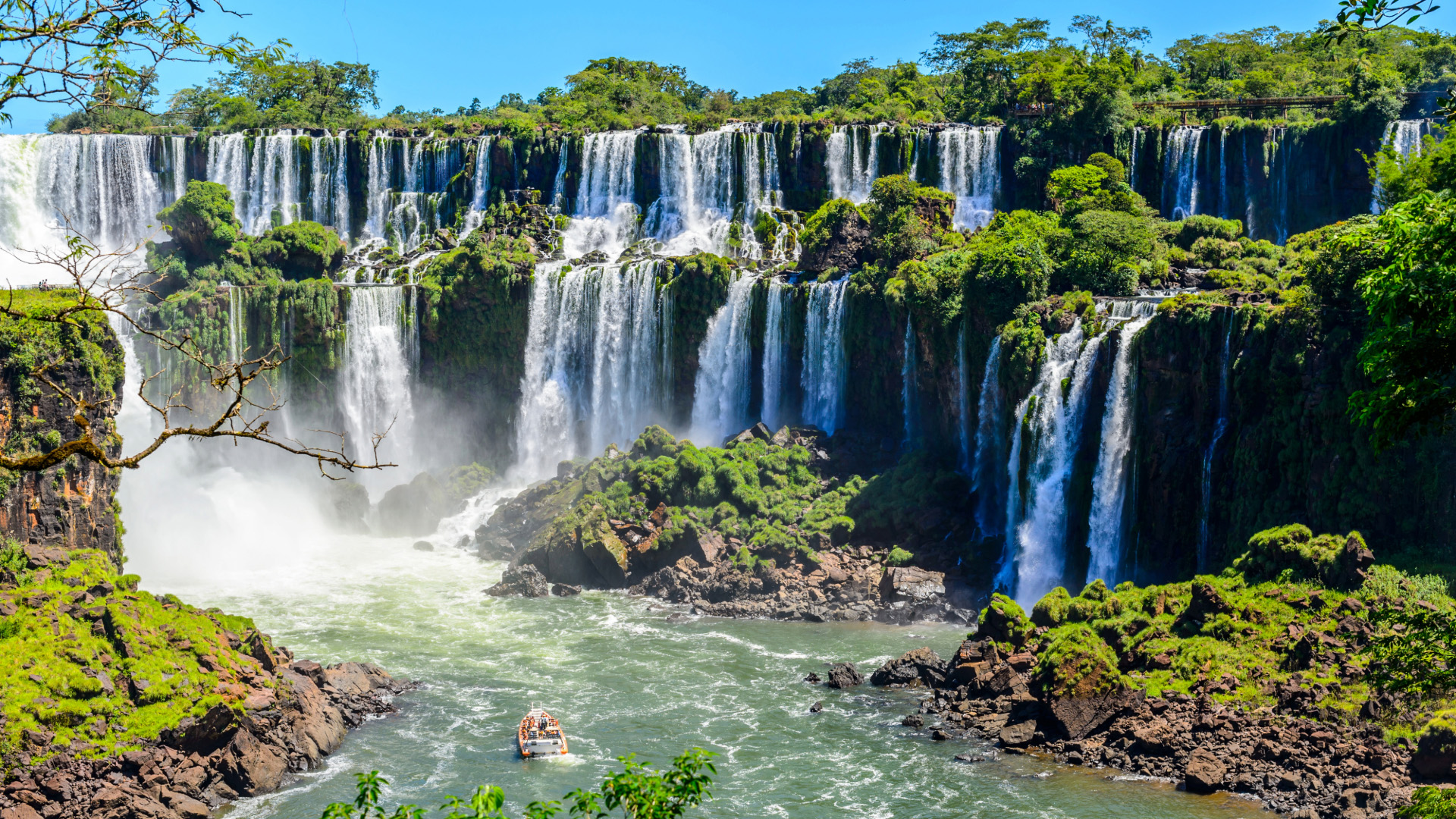 Several multi-level waterfalls above a jungle river with a boat in the river below