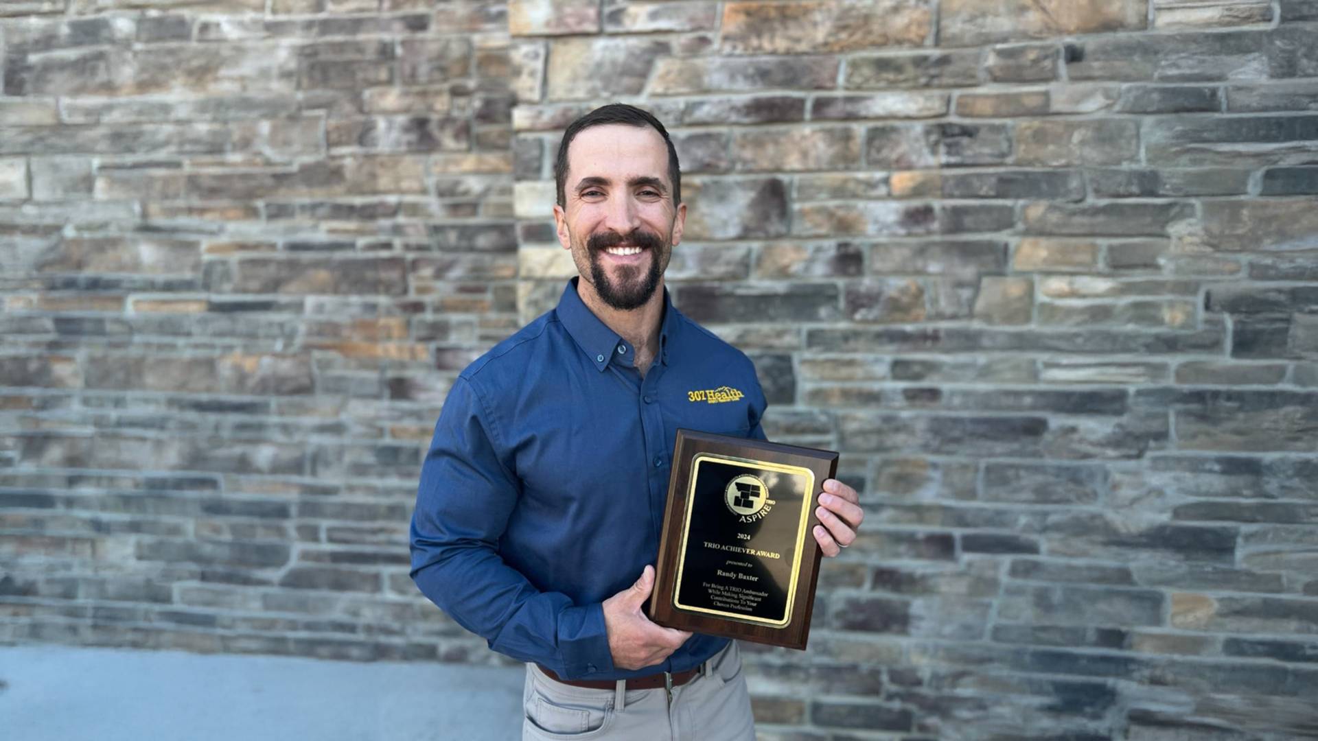 Randy Baxter in blue button down shirt and khaki pants holding a plaque